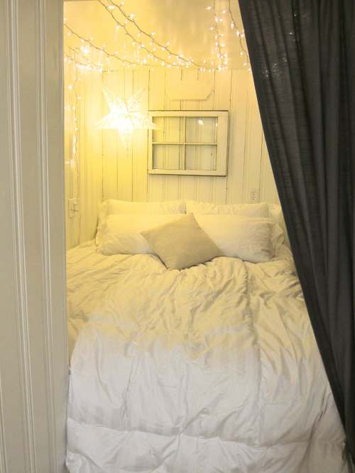 Cozy bedroom with white bedding, a decorative star, and string lights, framed by a dark curtain.