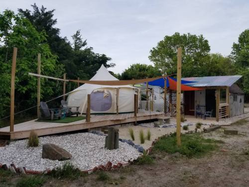 A cozy outdoor space featuring a yurt, colorful canopies, wooden deck, and seating area surrounded by greenery.