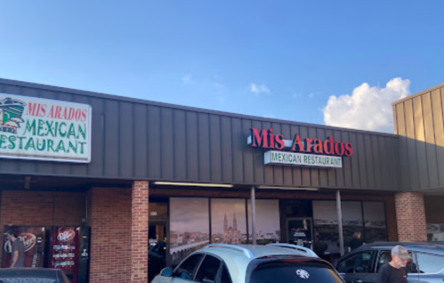 Exterior of Mis Arados Mexican Restaurant, featuring a sign and nearby parked cars under a blue sky.