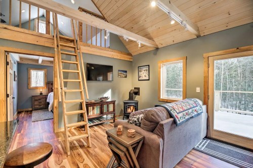 Cozy cabin interior with wooden accents, a staircase, and a view of the forest through large glass doors.