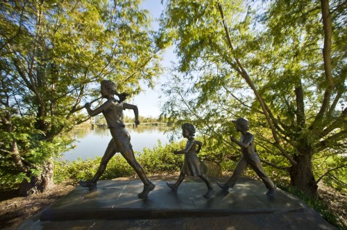 A bronze sculpture of a woman running with two children, surrounded by trees and a serene lake in the background.