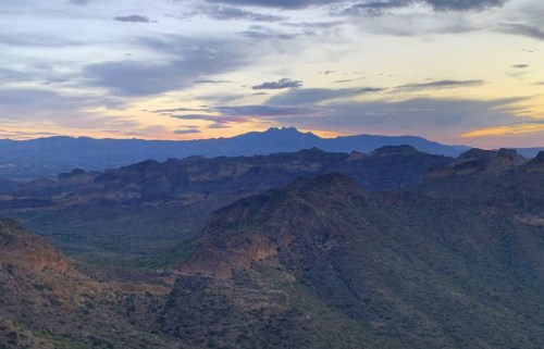 A scenic view of mountains and valleys at sunset, with a colorful sky and rugged terrain.