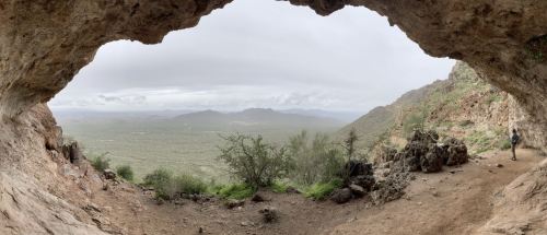 A panoramic view from inside a cave, overlooking a lush valley and distant mountains under a cloudy sky.