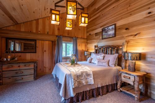 Cozy rustic bedroom with wooden walls, a log bed, decorative lamps, and a warm, inviting atmosphere.