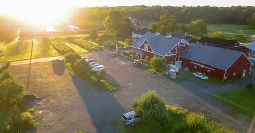 Aerial view of a red barn surrounded by greenery, with sunlight shining over a parking area and fields.