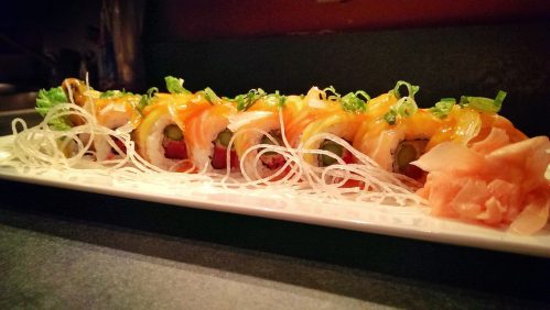 A plate of sushi rolls topped with salmon, garnished with green onions and served with pickled ginger.