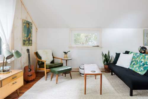Cozy living space with a green chair, guitar, plants, and a black sofa, featuring light walls and natural light.
