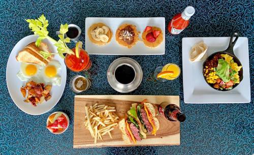 A colorful spread of breakfast and lunch dishes, including eggs, burgers, fries, and drinks on a blue table.