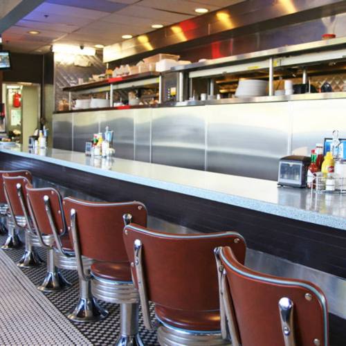 A diner interior featuring a long counter with metal stools and a shiny kitchen backdrop.