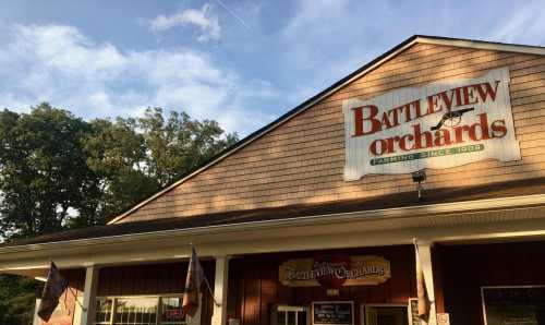 Exterior of Battleview Orchards building with a sign, surrounded by trees and a blue sky.