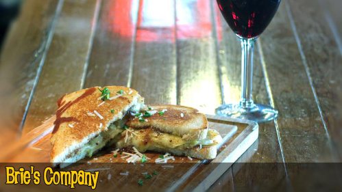 A toasted sandwich with filling on a wooden board, accompanied by a glass of red wine.