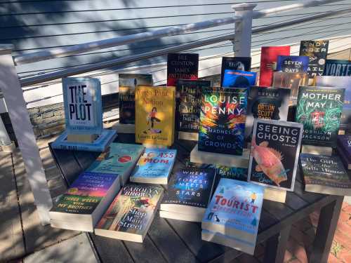 A collection of books displayed on a table outdoors, featuring various titles and authors.