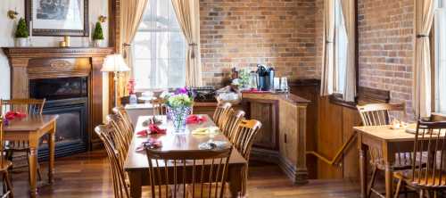 Cozy dining area with wooden tables, chairs, and a brick wall, featuring a fireplace and coffee station.