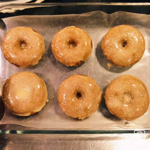 A tray of six glazed donuts, shiny and golden, arranged neatly on parchment paper.