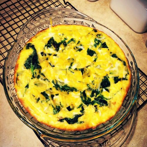A baked frittata with spinach and cheese, cooling on a wire rack in a glass dish.