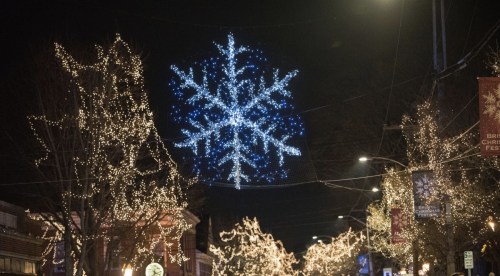 A street decorated with twinkling lights and a large illuminated snowflake hanging above.