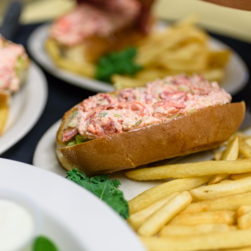 A lobster roll filled with creamy lobster salad, served with a side of golden French fries and garnished with lettuce.