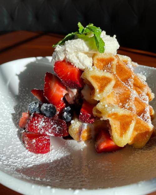 A plate of waffles topped with fresh strawberries, blueberries, whipped cream, and a sprinkle of powdered sugar.