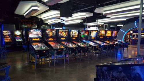 A row of colorful pinball machines in a modern arcade with bright lighting and a sleek design.
