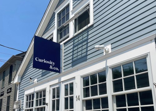 A blue building with a sign reading "Curiosity & Co." hanging above large windows.