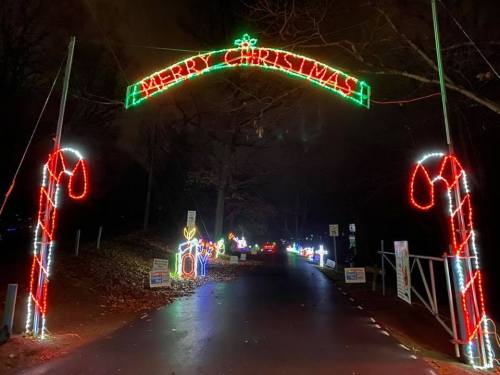 A festive archway reading "Merry Christmas" with colorful lights and candy cane decorations along a dark road.
