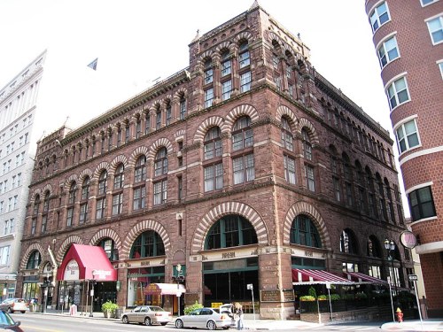 Historic brick building with arched windows and a red awning, located on a city street.