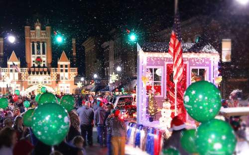 A festive night parade with colorful floats, snowflakes, and people holding green balloons, celebrating the holiday season.