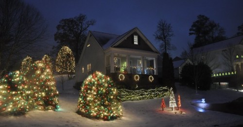 A cozy house decorated with colorful Christmas lights, surrounded by snow-covered trees and festive decorations.