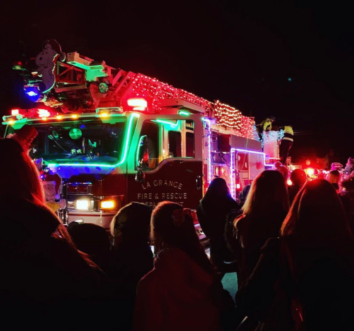 A brightly lit fire truck decorated for the holidays, surrounded by a crowd at night.