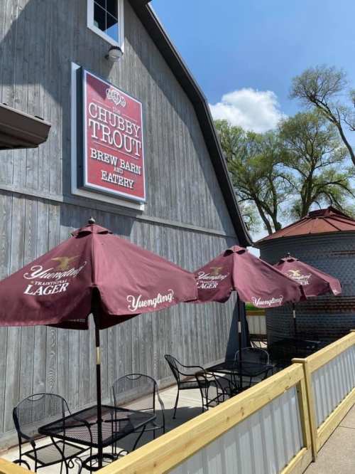 Exterior of Chubby Trout Brew Barn Eatery with umbrellas and seating in front of a rustic wooden building.