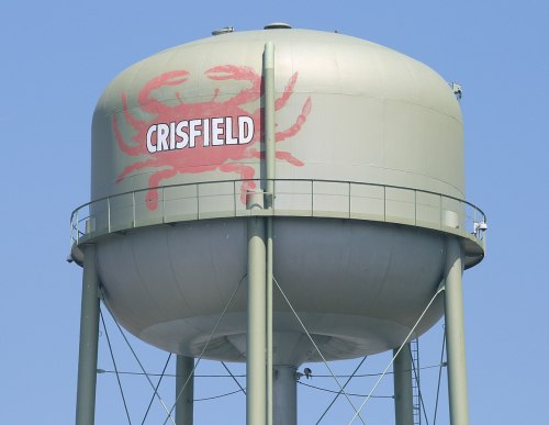 Green water tower with a red crab design and the word "CRISFIELD" painted on it against a clear blue sky.