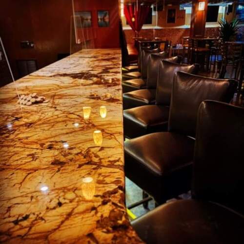 A dimly lit bar with a polished marble countertop and black leather chairs arranged along the side.