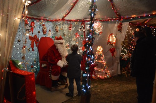 A festive scene with Santa Claus sitting in a decorated tent, surrounded by colorful lights and holiday decorations.