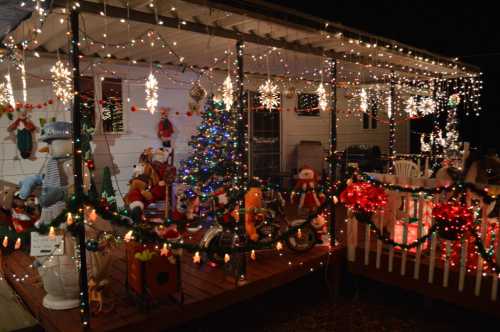 A festive porch decorated with colorful lights, a Christmas tree, and various holiday decorations and figures.