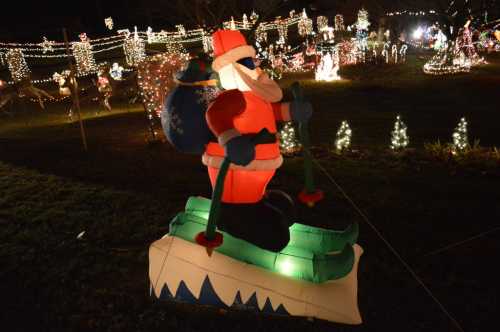 Inflatable Santa skiing with a bag of gifts, surrounded by colorful holiday lights in a festive outdoor display.