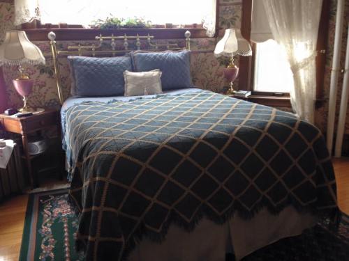 A cozy bedroom featuring a brass bed with a patterned quilt, two lamps, and floral wallpaper.