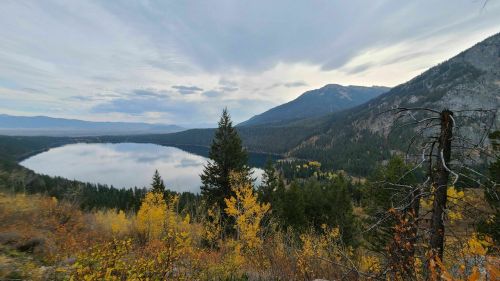 A serene lake surrounded by mountains and autumn foliage under a cloudy sky.
