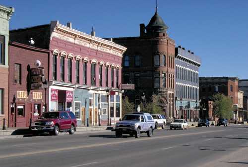 Historic buildings line a street in a small town, featuring a mix of architectural styles and parked cars.