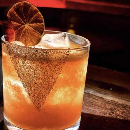 A close-up of a cocktail with a salted rim, garnished with a slice of lime, served in a clear glass.