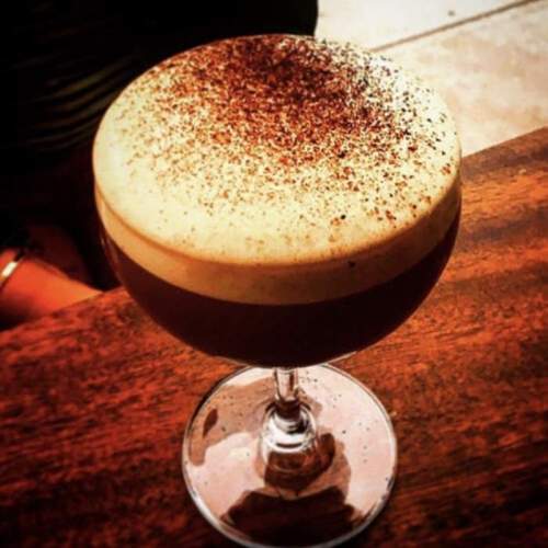 A close-up of a coffee cocktail topped with frothy cream and cocoa powder, served in a stylish glass.