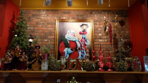 A festive display featuring a Santa portrait, Christmas trees, decorations, and holiday-themed figurines on a mantel.