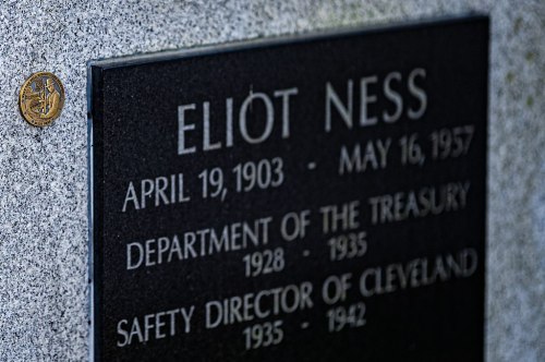 Close-up of a gravestone for Eliot Ness, featuring his name and dates, with a coin placed on the stone.
