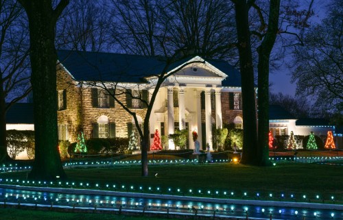 A beautifully lit mansion surrounded by trees, decorated with colorful holiday lights at dusk.