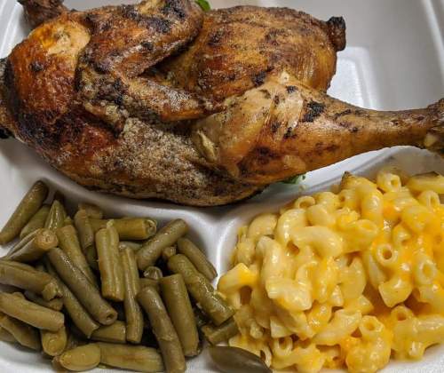 A plate with a roasted chicken, green beans, and creamy macaroni and cheese in a takeout container.