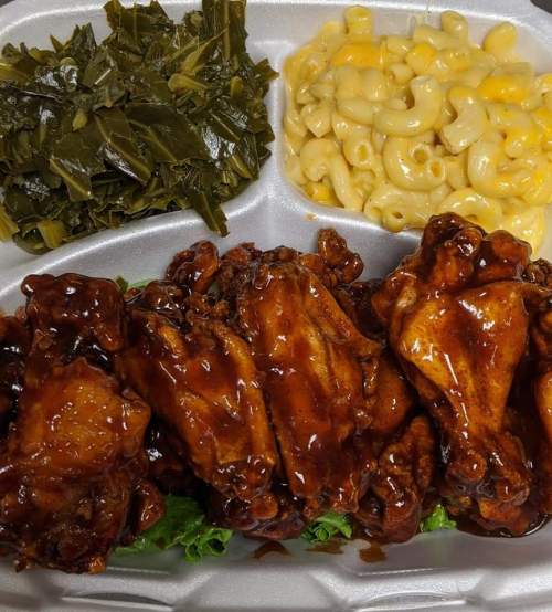 A plate of glazed chicken wings, collard greens, and macaroni and cheese, served on a divided tray.