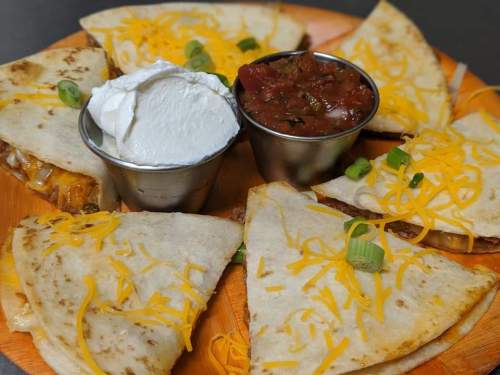 A plate of quesadillas with cheese, served with sour cream and salsa in metal cups, garnished with green onions.