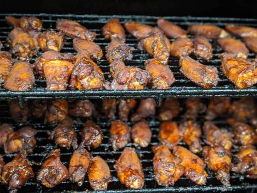 Grilled chicken wings coated in a rich, dark sauce on a barbecue grill.