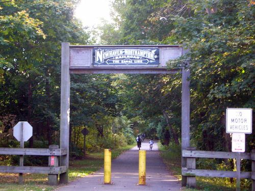 A wooden archway marks the entrance to a trail, with a sign for the Northampton Railroad and a no motor vehicles sign.