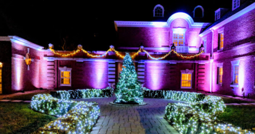 A beautifully lit building at night, adorned with colorful lights and a decorated tree in a landscaped garden.