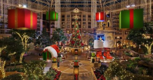 A festive indoor scene featuring a large Christmas tree, holiday decorations, and colorful gift boxes hanging from above.
